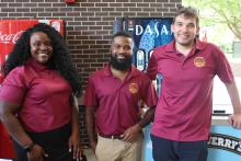 three students posing and smiling with COGS shirts