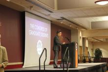 person standing behind a podium and next to a presentation