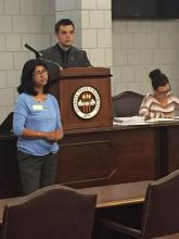 student speaking in front of a podium as students behind a podium look on