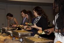 people lining up to select food from a buffet