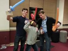 two men posing holding baloon swords with a smiling child