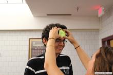 man looking up as a sticky note is placed on his forehead