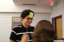 man looking up as a sticky note is placed on his forehead