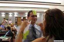 man looking up as a sticky note is placed on his forehead